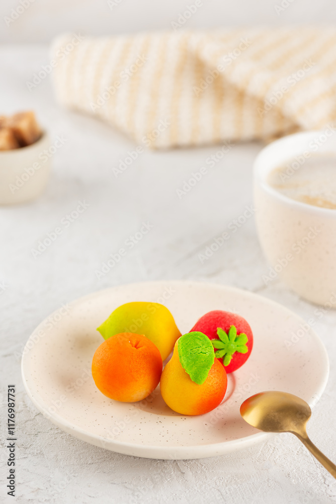 Marzipan candies in the form of fruits: pear, tangerine, lemon and strawberry in a plate with a cup of coffee. Vertical orientation. Marzipan candies in the form of fruits: pear, tangerine, lemon and strawberry in a plate with a cup of coffee. Vertical orientation.