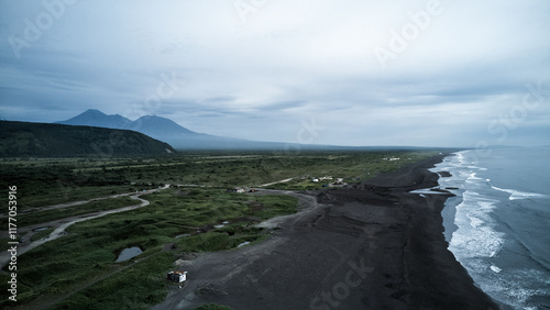 Aerial view of Khalaktyrsky Beach. A tranquil scene with a black sand beach, gentle waves, and lush mountains under a cloudy sky for a perfect getaway photo