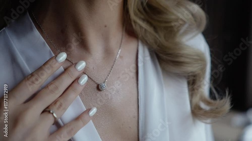 a beautiful young bride in a white dress with an open neckline hangs pearl jewelry on her neck and strokes her body, morning preparations before the wedding ceremony