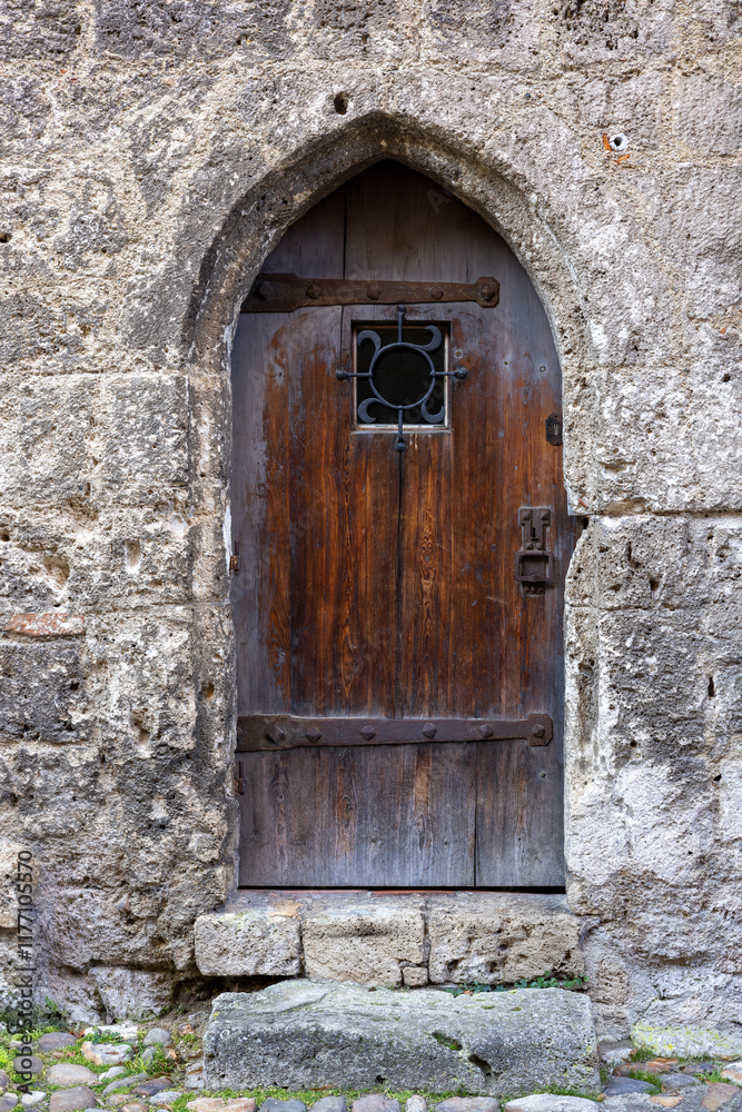An ancient wooden door with iron reinforcements and a small window, set within a stone wall of a medieval castle, reflecting timeless craftsmanship and historical charm. An ancient wooden door with iron reinforcements and a small window, set within a stone wall of a medieval castle, reflecting timeless craftsmanship and historical charm.