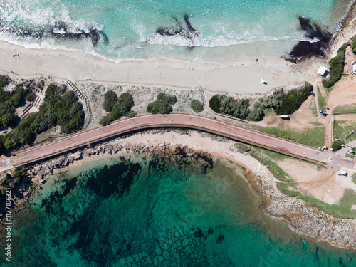  The isthmus connecting Capo Testa to mainland Sardinia, featuring turquoise waters, sandy beaches, and a coastal road surrounded by lush greenery and rocky shores.