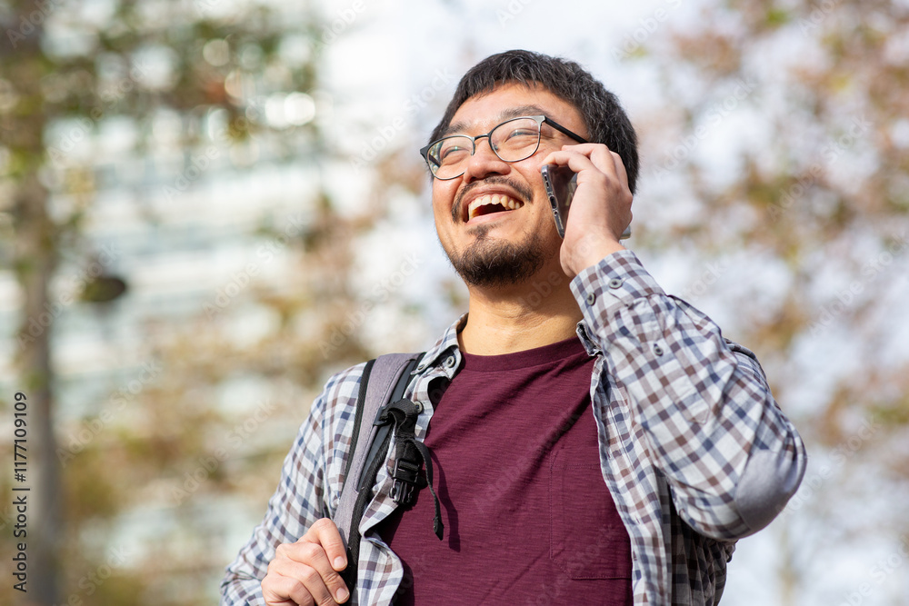 Taiwanese man using phone with a smile in an outdoor setting Taiwanese man using phone with a smile in an outdoor setting