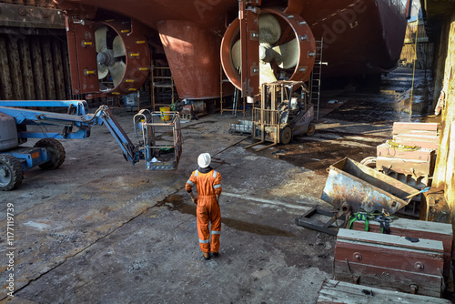 Male worker standing at the bottom of the dry dock, with ship inside, on the blocks.