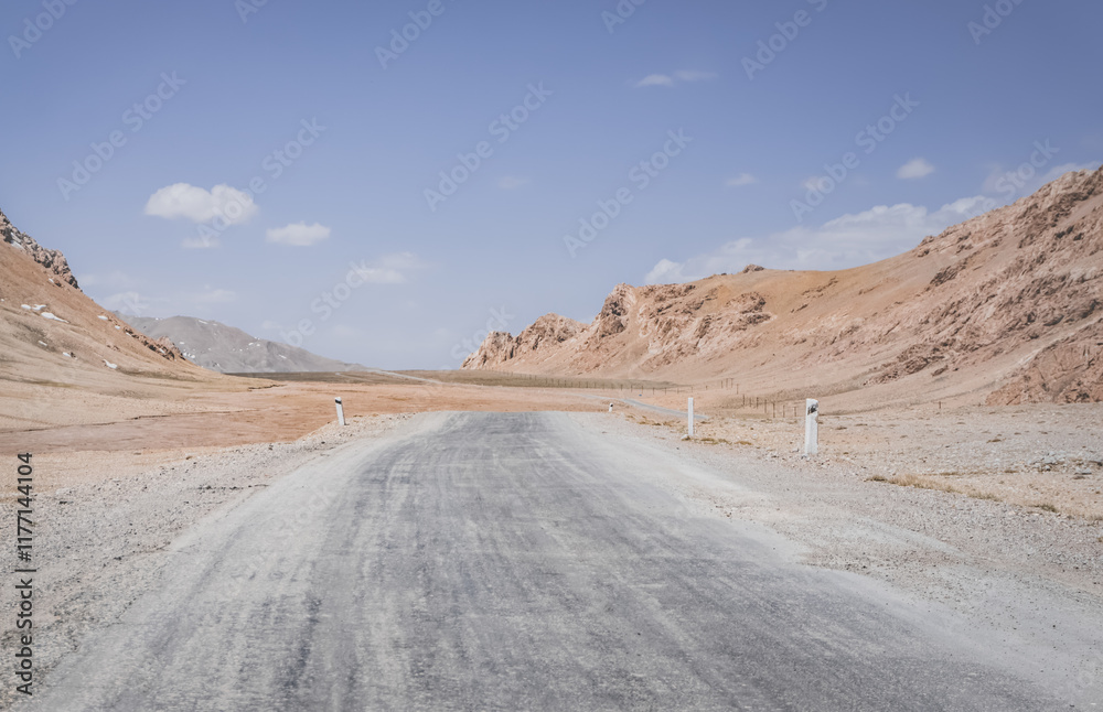 Asphalt road of the Pamir Highway in the valley of the Tien Shan Mountains in Tajikistan in the Pamirs, landscape in the high desert mountains for background, the road goes into the distance Asphalt road of the Pamir Highway in the valley of the Tien Shan Mountains in Tajikistan in the Pamirs, landscape in the high desert mountains for background, the road goes into the distance
