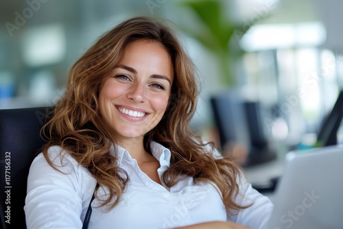 Free Download A joyful young woman with wavy hair is smiling while working at her desk, capturing a sense of professionalism and happiness in a modern office environment. - GFXLoad