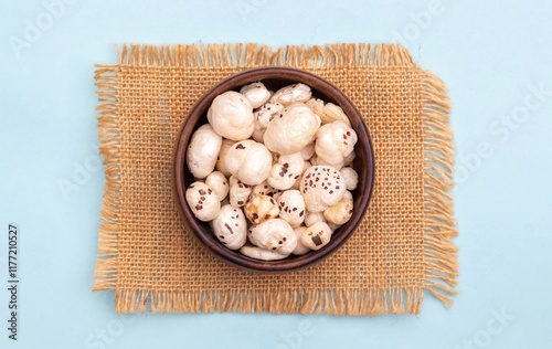 Top View of Fox Nut or Makhana in a Wooden Bowl on Burlap Fabric Isolated on Light Blue Background with Copy Space, Also Known as Lotus Seed Pop, Euryale Ferox or Gorgon Nut