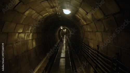 Panning shot of an underground tunnel with segmented concrete ceiling, overhead lights and wet floor. Inside Fort de Mutzig fortess, now a museum.  photo