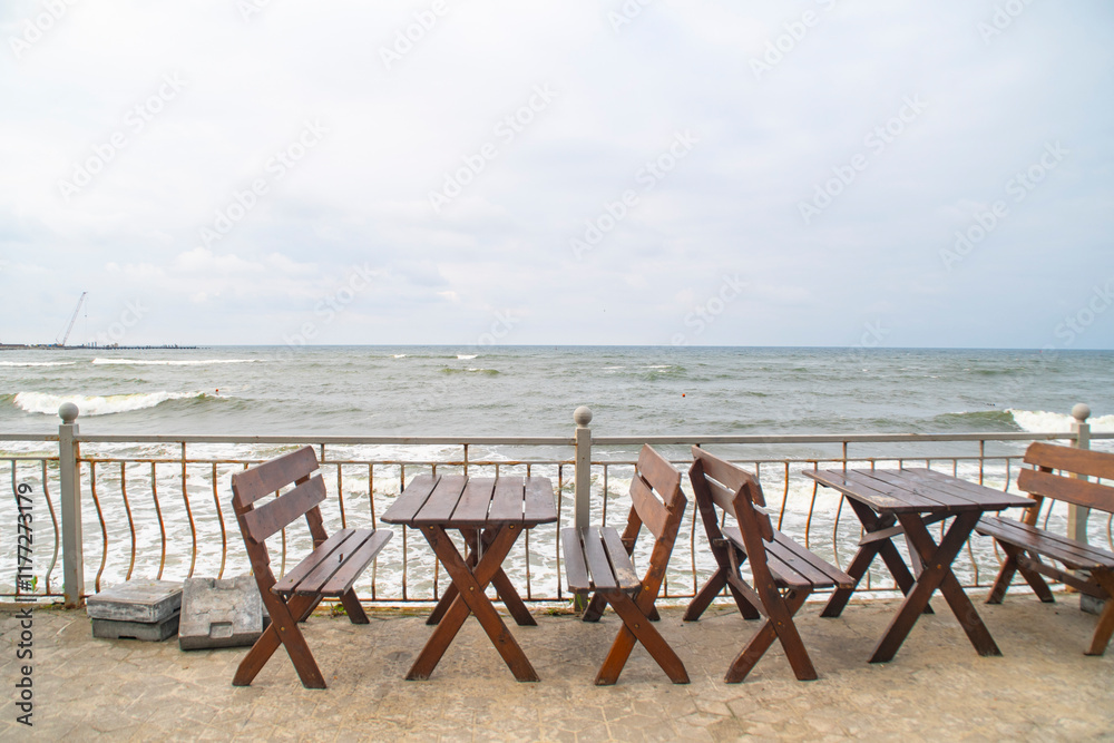 Empty tables and chairs of a street cafe near the sea. Cold weather on the embankment. Empty tables and chairs of a street cafe near the sea. Cold weather on the embankment.