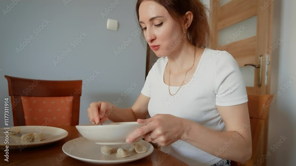 Young woman eating dumplings during meal. Female enjoying homemade dish with spoon and focused expression. Lady savoring food while sitting at dining table in relaxed atmosphere Young woman eating dumplings during meal. Female enjoying homemade dish with spoon and focused expression. Lady savoring food while sitting at dining table in relaxed atmosphere