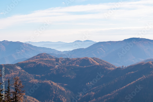 Scenic view of hilly landscape and mountains of Graz Highland and Glein Alps shrouded in mist seen from Pribitz, Hochschwab Alps, Styria, Austria. Rolling hills covered in forest vibrant autumn colors photo