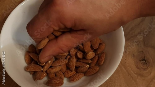 Man takes handful of almonds from white bowl. Nutritious snack, healthy food