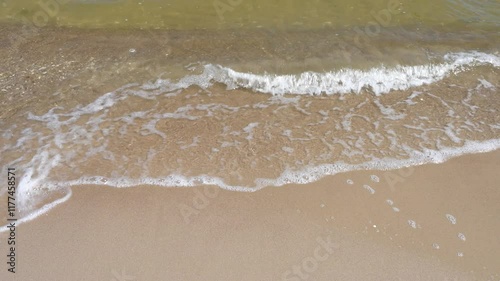 Sandy shore of  Baltic Sea,  wave rolls gently on  wet sand, leaving subtle sheen of water photo