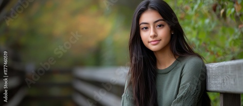 Obraz na płótnie High school senior portrait of a teenage girl with long dark hair, posing confidently outdoors on a wooden bridge surrounded by green and autumn-colored foliage. w salonie