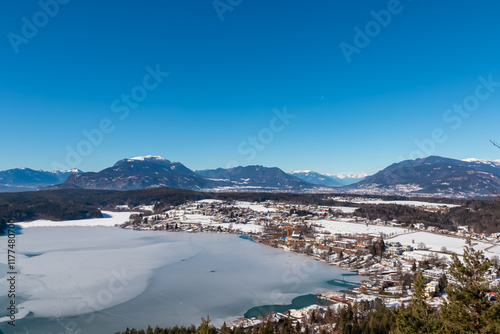 Scenic view on frozen Lake Faak from Taborhoehe in Carinthia, Austria, Europe. Surrounded by high snow capped mountains of Karawanks and Julian Alps. Alpine Landscape in frosty winter, Austrian Alps photo