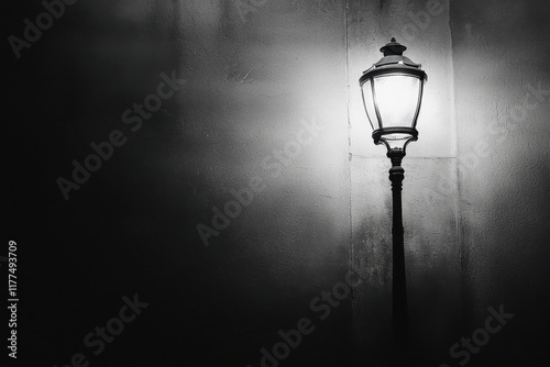 Old fashioned street lamp casting light on a dark alley wall in black and white