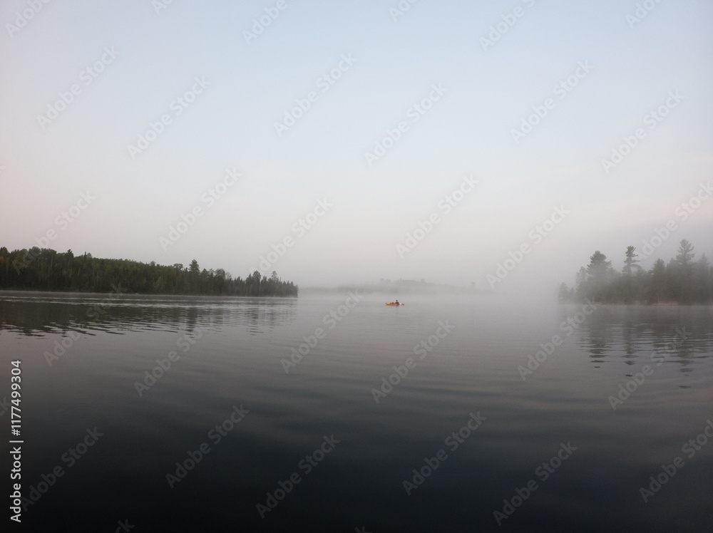 Fototapeta premium Solo kayak paddling in a misty morning on the lake in the Boundary Waters (BWCA)