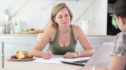 Two positive middle-aged women having business conversation while sitting at the kitchen-table 