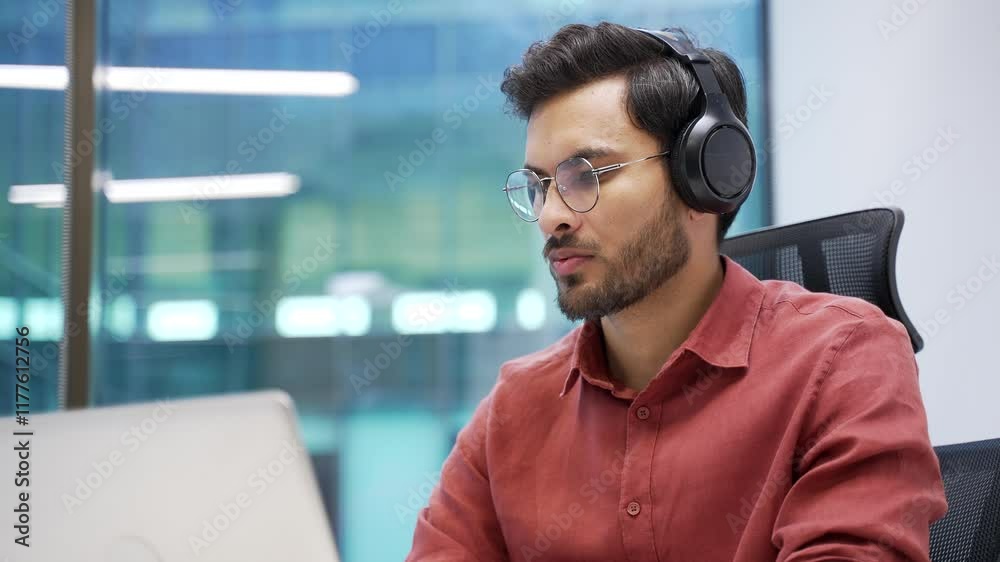 Focused IT specialist in wireless headphones works on a laptop sitting at workplace in business office. Handsome coder writes code. Developer is programming, busy with a project on computer. Close up