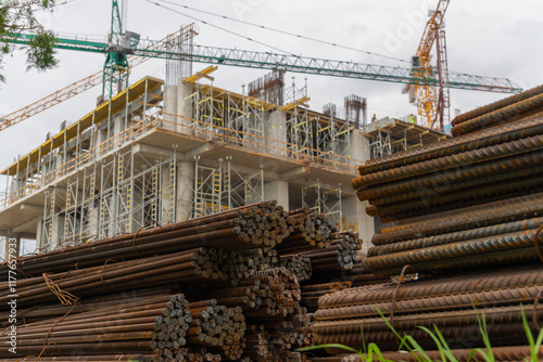 Obraz na płótnie Steel rods stacked together at a construction site, with construction workers and a crane visible working on the building in the background w salonie