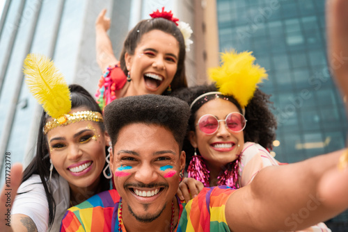 Joyful friends celebrating Brazilian Carnival in colorful costumes outdoors. Cheerful group of young adults with vibrant makeup enjoying urban Carnaval in the street