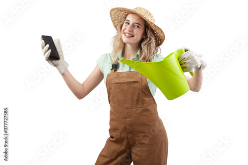 Smiling woman wearing an apron, hat and gloves for gardening holding a watering can, isolated on a white background showing smartphone. Online gardening shopping for spring and garden work photo