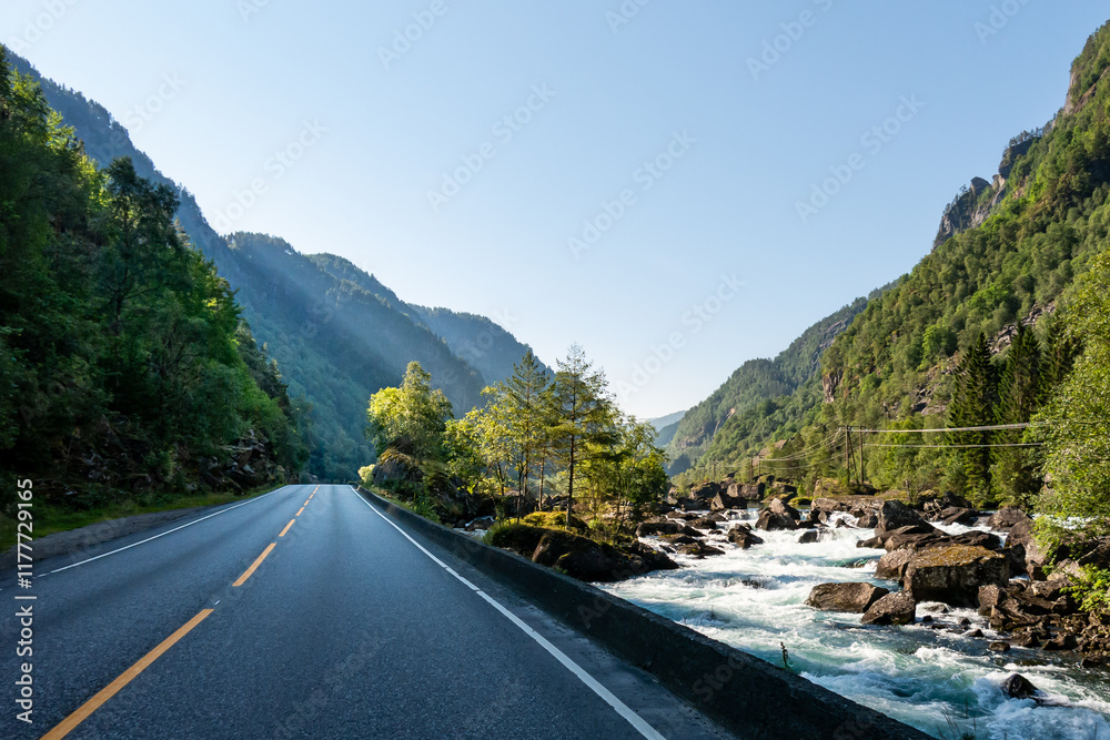 Majestic river flows alongside a mountain road under bright blue skies during midday. Majestic river flows alongside a mountain road under bright blue skies during midday.