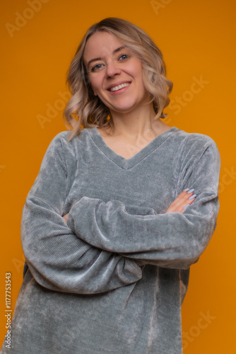 Smiling woman in a gray cozy sweater with arms crossed, standing against a vibrant yellow background. Warm, approachable, and confident look, perfect for lifestyle and casual stock photography. photo