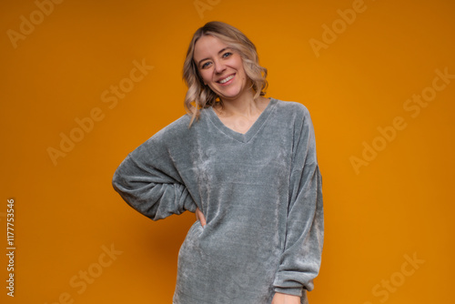 A cheerful woman with blonde hair in a cozy gray sweater poses confidently against a vibrant yellow background, exuding warmth, positivity, and a modern casual style. photo