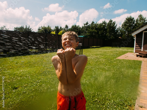 Boy enjoys water spray while playing in backyard under sunny sky. photo