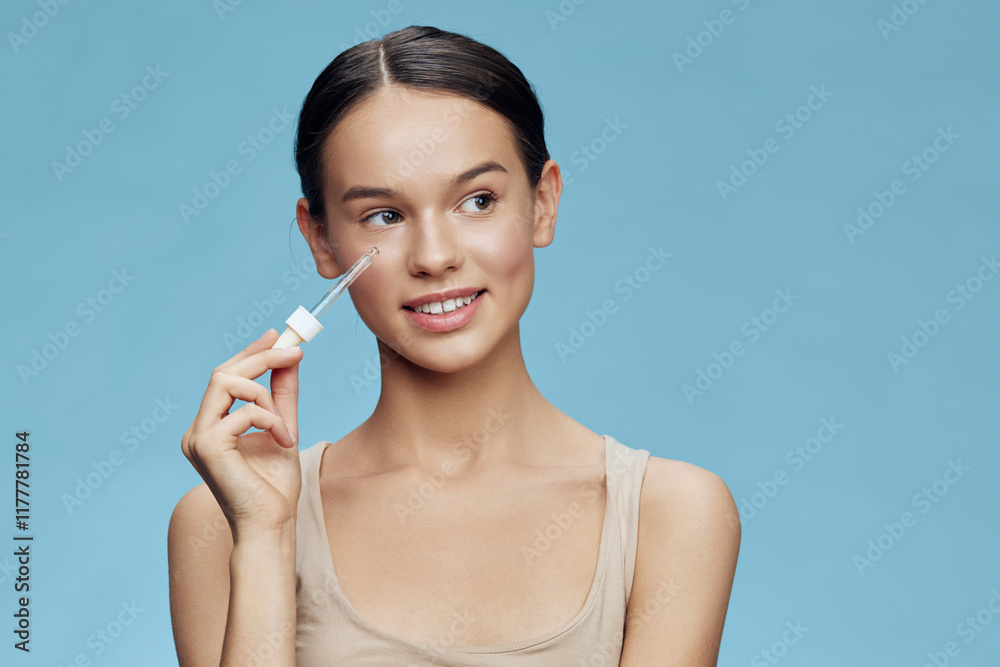 Young woman applying serum for skincare with a bright blue background, showcasing a healthy complexion and a joyful expression, representing beauty and self care Young woman applying serum for skincare with a bright blue background, showcasing a healthy complexion and a joyful expression, representing beauty and self care