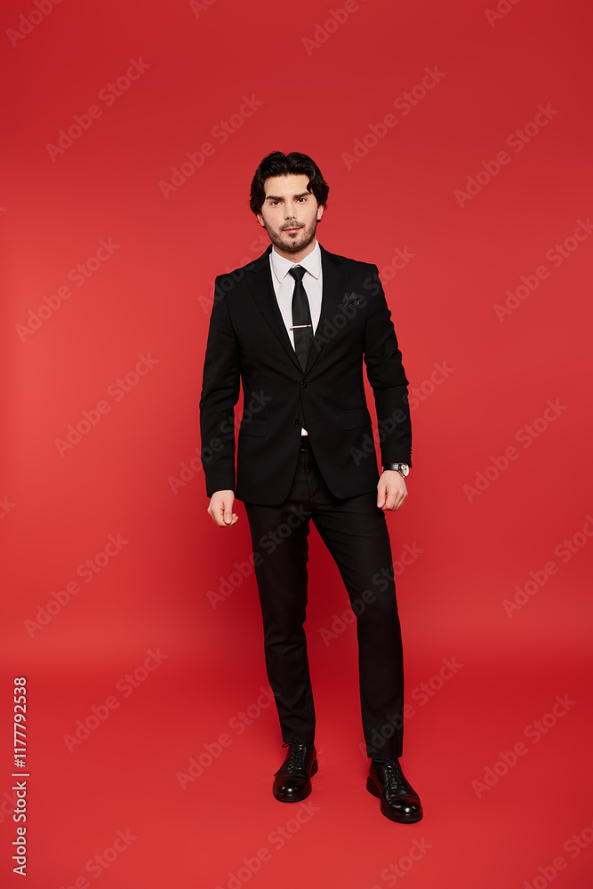 Young handsome man confidently posing in a stylish suit against a vibrant red backdrop Young handsome man confidently posing in a stylish suit against a vibrant red backdrop