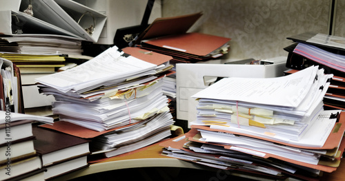 Messy Desk with Books Binders Files and Papers Stacked up High in a Disorganized Office Space