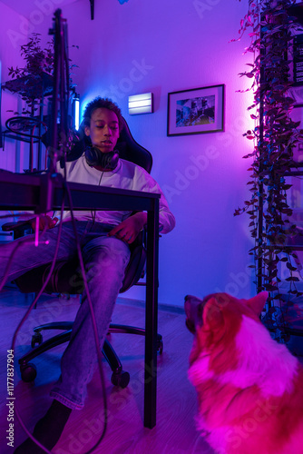 Young Man Relaxing at Gaming Desk with Dog Under Neon Lights photo