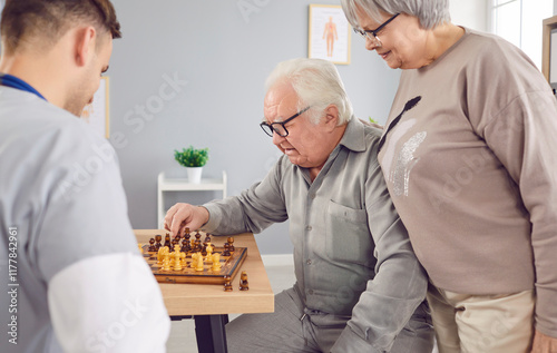 Young male nurse and old man playing chess enjoyable activity, taking social care. Man monitoring male, female resident of nursing home or patient in hospital, clinic, maintain elderly health, safety photo