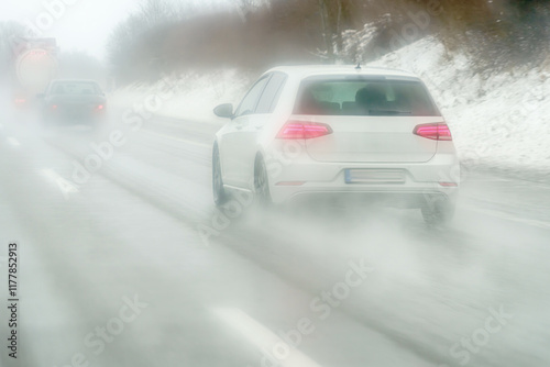 A white car moves along the highway during the rain. Water splashes from the wheels.