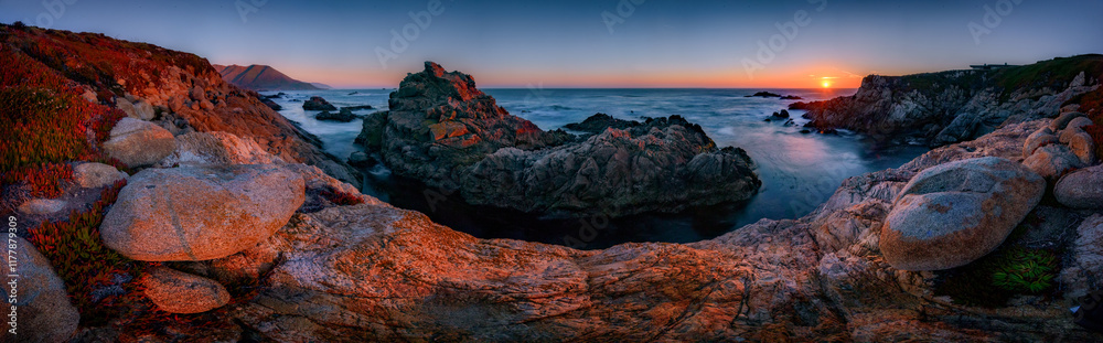 Fototapeta premium Big Sur Pinnacle Rock panorama at sunset. Sun on distant Pacific Coast horizon.