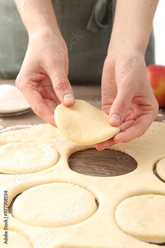 Woman making pirozhki (stuffed pastry pies) at wooden table, closeup photo