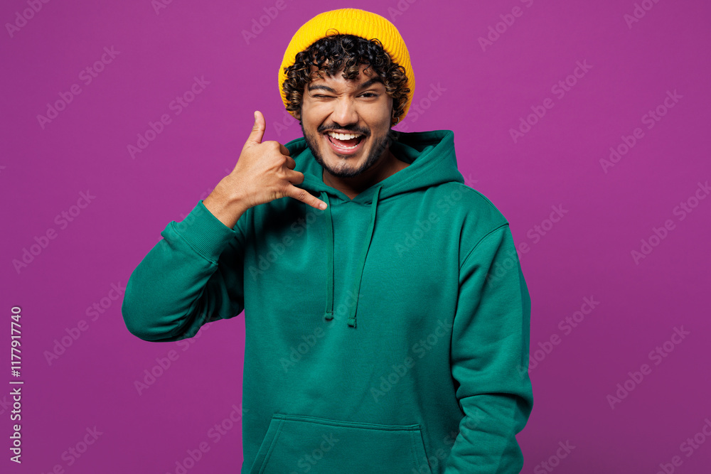 © ViDi Studio - Young happy Indian man he wear green hoody yellow hat casual clothes doing phone gesture like says call me back wink blink eye isolated on plain purple background studio portrait. Lifestyle concept. © ViDi Studio - Young happy Indian man he wear green hoody yellow hat casual clothes doing phone gesture like says call me back wink blink eye isolated on plain purple background studio portrait. Lifestyle concept.