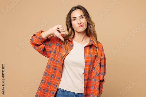 Young sad disappointed dissatisfied woman she wears orange shirt casual clothes showing thumb down dislike gesture isolated on plain pastel light beige background studio portrait. Lifestyle concept.