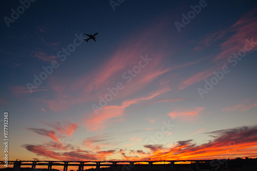 Airplane flying over a vibrant sunset sky near a city bridge photo