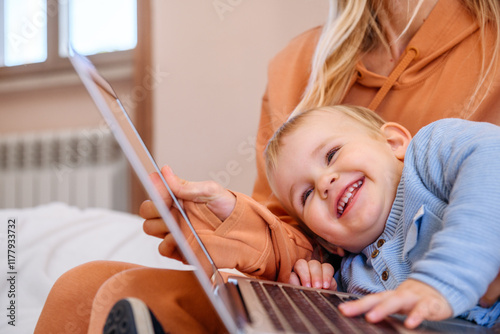 Smiling child lay down on laptop while mom works photo