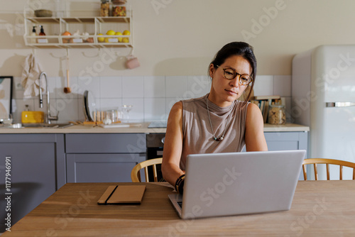 Woman using laptop working remotely from kitchen photo