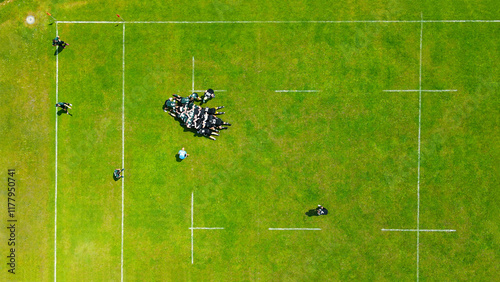 Aerial View of Rugby Scrum on Green Field. A top-down aerial view of a rugby match in progress, highlighting a scrum formation on a vibrant green field with white markings.
