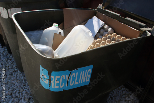 Recycling bin filled with cardboard and plastic waste outdoors.