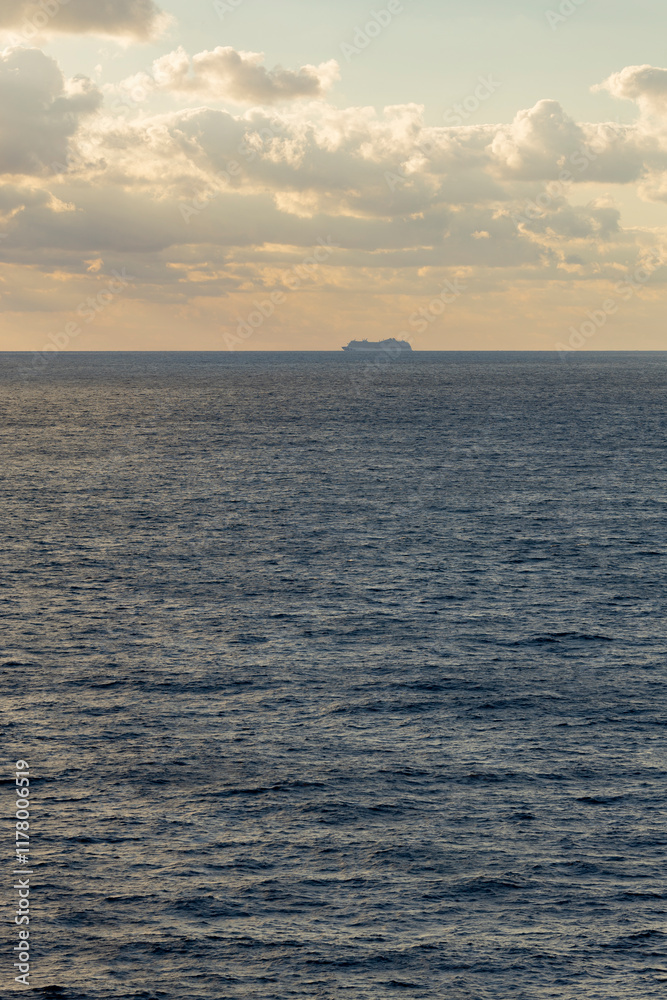 Obraz premium vertical sea view with beautiful water, horizon and warn golden sky, and the silhouette of a cruise ship in the distance