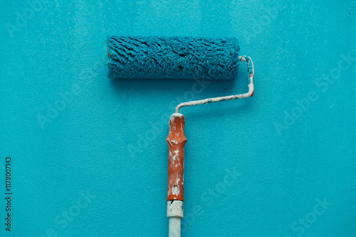 A paint roller rests on a blue wall