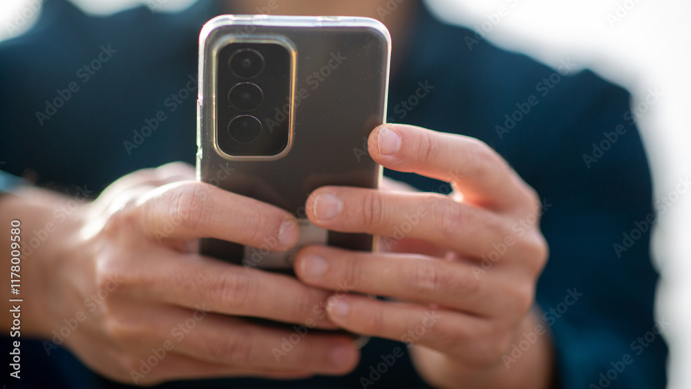 Close-up view of hands holding a phone outdoors with blurred teal shirt in the background Close-up view of hands holding a phone outdoors with blurred teal shirt in the background