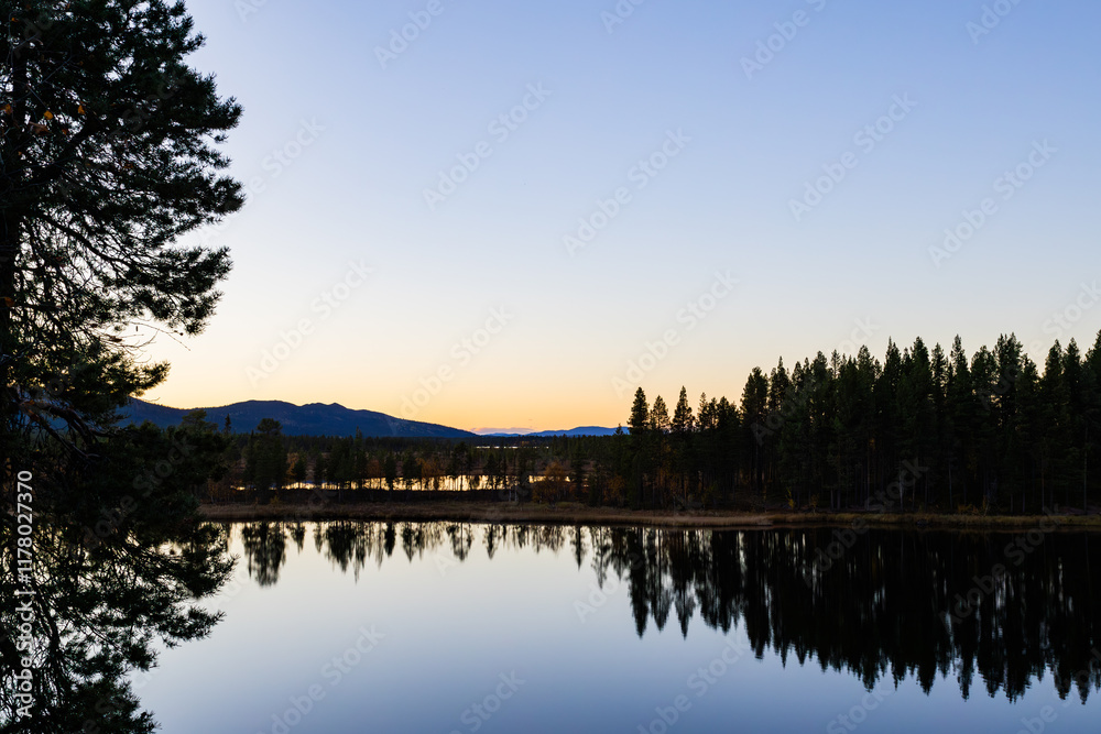 A peaceful sunset over a lake in Lapland, Sweden, with the reflection of trees in the still water. A peaceful sunset over a lake in Lapland, Sweden, with the reflection of trees in the still water.