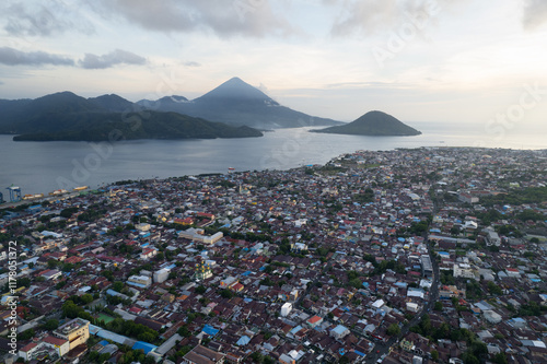 Aerial view of a coastal Indonesian city with volcanoes in background
