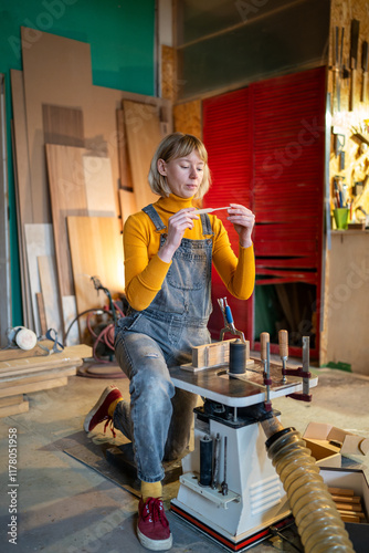 Handywoman joiner turns blanks for wooden knives on lathe, inspecting work in carpenter workshop. Female master custom designs, artisan expertise, handmade tools quality, small business and occupation
